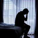 a silhouette of a lonely man sitting on a bed in the dark holding one hand on his head