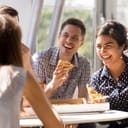 A group of people at desk eating pizza and laughing