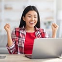 A happy, smiling young woman with fists in the air looking at a laptop