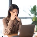 A fatigued young businesswoman massages her nose, visibly exhausted from work.