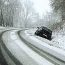 A snowed over road and a car in a ditch with skid marks behind it