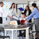 male businessman feeling overwhelmed in a noisy office with colleagues assigning him multiple tasks