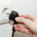 Female hand unplugging a plug from a socket, metaphor for saving electrical energy