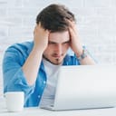 Stressed young man holding his head while looking at a laptop