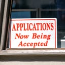 Sign reading "APPLICATIONS Now Being Accepted" displayed in a window