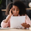 A worried woman holding her head a looking at a piece of paper