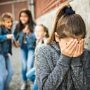 A sad girl experiencing intimidation during an elementary school bullying moment in the schoolyard.