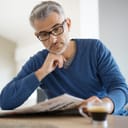 Man sitting at table reading newspaper with a cup of coffee