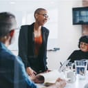 Happy young businesswoman leading a briefing in an office. Group of creative businesspeople attending their morning meeting in a modern workplace. Businesspeople working together.