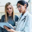 Attentive female doctor explaining treatment details to a female patient using a tablet during a consultation.