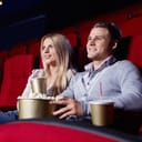 A couple watching a movie in a cinema holding popcorn and soft drinks