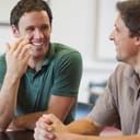 A closeup of two men sitting at a table talking