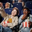 Two friends sitting and eating popcorn in a cinema