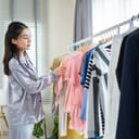 young Asian woman in pajamas selecting clothes from a closet rack in her bedroom