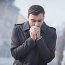 Man in cold weather blowing into clutched fists