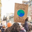 Female climate protestor holds sign reading: "System Change, Not Climate Change"