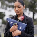 a mourning woman with a rose and flag at a cemetery memorial service