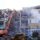 Building being demolished by an excavator