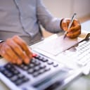 Close-up of a person drafting a payroll compensation check, with a bank paycheck and calculator in the focus.