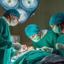 Three experienced surgeons performing a surgery in the hospital, wearing green gowns.