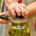 close-up of fresh cucumbers being preserved in glass jars and sealed with a seamer