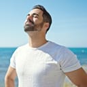 Young hispanic man breathing with closed eyes at seaside