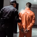 The rear view of a prison officer leading a prisoner in handcuffs