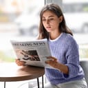A young woman reading a newspaper at a cafe