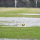 A green softball sits on a waterlogged field as it's raining.