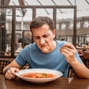 dissatisfied unhappy customer of the restaurant sniffs the disgusting smell of a bowl of soup with spoiled ingredients and is going to complain to the chef