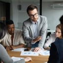 young confident businessman talking to his diverse team of four during an office meeting