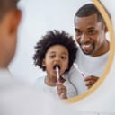 A father and his child looking at themselves in the mirror brushing teeth