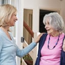 A middle aged woman talking to a senior woman at a doorstep of a house
