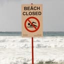 A Beach Closed sign on a beach with a restless sea in the background