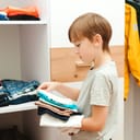 Close-up of a little boy sorting folded clothes in his wardrobe.