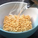 Boiling water being poured over dried noodles