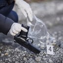 Investigator collecting a handgun off the ground to be put into evidence bag