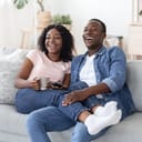 joyful African couple drinking tea and watching a movie at home