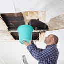 a man collecting water in a bucket from a leak in the damaged ceiling