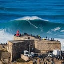 Surfer riding huge wave near the Fort of Sao Miguel Arcanjo Lighthouse in Nazare, Portugal