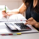 A woman sorting her finances using a calculator and writing it in a register