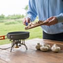 A person throwing fresh mushrooms into a pan placed on a gas camp stove