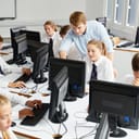 A group of teenage students focused on their studies in an Information Technology classroom, with the professor explaining the task.