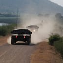 A convoy of military trucks driving down a dusty road
