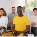 Portrait of focused African American man participating study session, sitting in auditorium with multiethnic group of men of various ages listening to lecturer with interest
