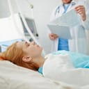 an unconscious woman lying a hospital bed with a doctor standing by