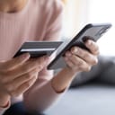 Close-up of a woman's hands as she uses a credit card and smartphone to make an online payment.