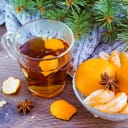A cup of tea with orange peels next to a glass bowl full of oranges and Aniseed