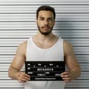 Arrested beaten man posing for a front-view mugshot with a placard