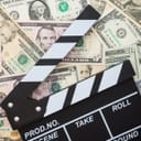 Clapperboard placed on pile of dollar bills